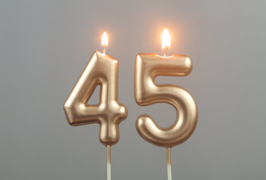 Burning gold birthday candles on gray background, number 45