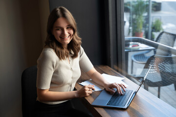 Shot of glad female businessperson with laptop waiting for coffee in coffee bar.