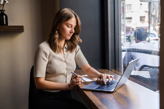 Shot of female businessperson using laptop and waiting for coffee in coffee bar.
