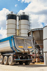 Large dump truck near the concrete factory. Car tonar for transportation of heavy bulk cargo. Provision of crushed stone and gravel for concrete production.