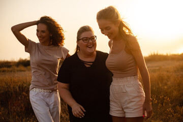 group pf three friends, plus sizewith two thin girls spend happy time together in the nature. Beautiful overweight and strong women have fun, enjoy the momet of sunset .