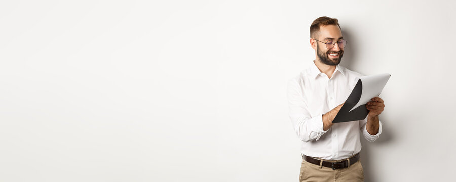 Man Looking Satisfied While Reading Documents, Holding Clipboard And Smiling, Standing Over White Background