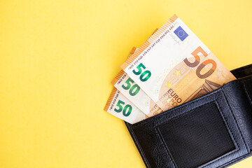 Fifty euro banknotes inside a black wallet on yellow background, cash paper currency, payment, earning and savings, european currency, money and finance concept