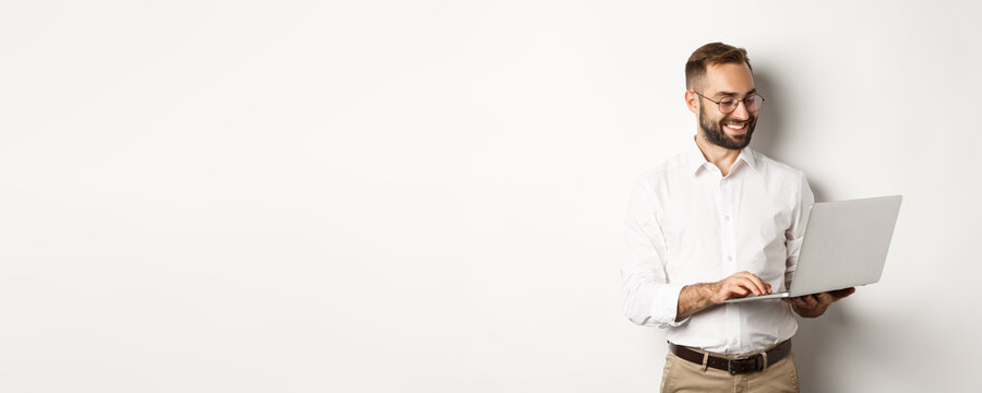 Business. Handsome Businessman Working On Laptop, Answering Messages And Smiling, Standing Over White Background