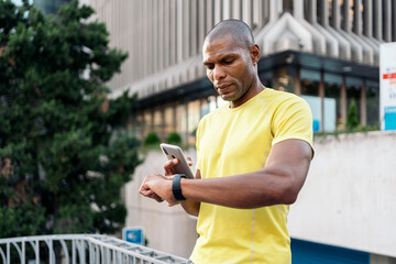 Adult man synchronizing mobile phone and smartwatch to do sports in the city.