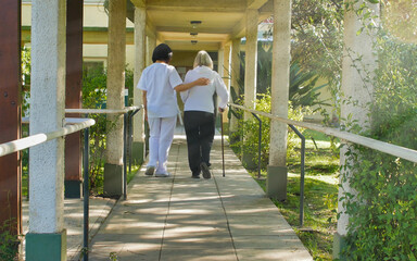 Asian doctor helping elderly retired woman with walker stick in the hospital yard. Rehabilitation concept