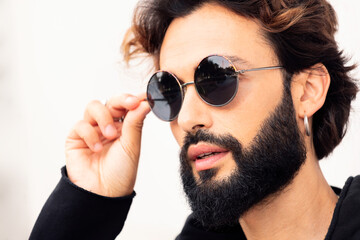 close up portrait of a beautiful young man with beard putting on sunglasses, concept of urban lifestyle and stylish clothing