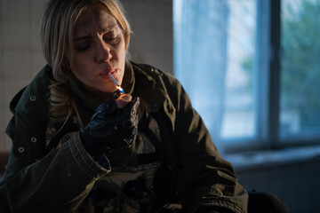 Special female soldier after the fight sitting in ruined building smoking cigarette staring at the...
