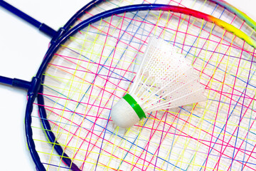 Top view of shuttlecock ball on colorful badminton rackets for kids. Close-up of badminton rackets and ball on isolated white background. Fun, sport, activity concept.