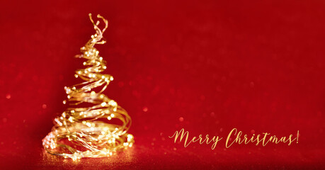 defocused christmas tree from the golden xmas lights on red background. Copy space. Merry Christmas text card. Blurred silhouette