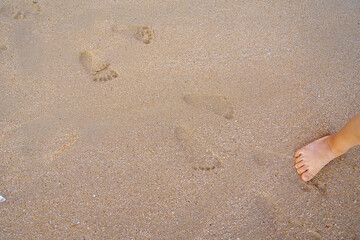 A child's foot and his footprints on the beach at dusk