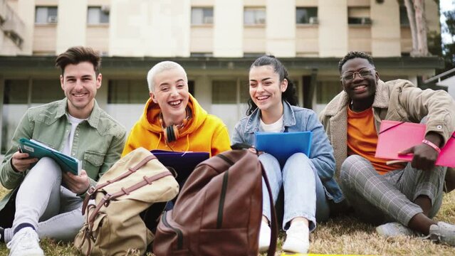 A group of four diverse teenage students smilind and laughing sitting on lawn and looking at camera at university campus. Two gitls and two boys having fun at park in front of the high school