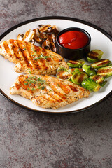 Healthy food grilled chicken fillet with Brussels sprouts, mushrooms and spicy tomato sauce close-up in a plate on the table. vertical