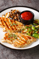 Grilled chicken fillet with Brussels sprouts, mushrooms and spicy tomato sauce close-up in a plate on the table. vertical