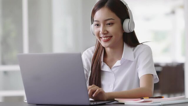 Slow motion happy Asian beautiful woman listening music with headphones while working with laptop computer.