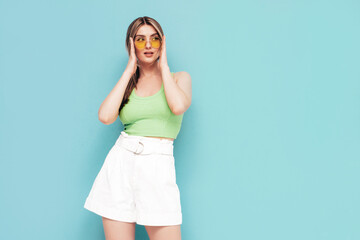 Portrait of young beautiful smiling female in trendy summer shorts clothes. Carefree woman posing near blue wall in studio. Sexy positive model having fun indoors. Cheerful and happy