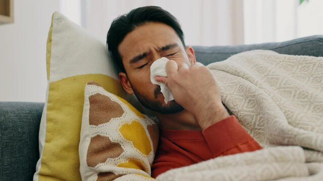 Flu, sick and cold man sneezing, blowing and cleaning runny nose with tissues while ill with covid, sinus and allergies on home sofa. Fatigue guy in isolation, corona virus risk and health problems