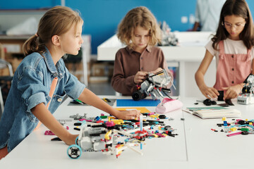 Group of youthful schoolkids standing by table with details of constructor and creating new robots...