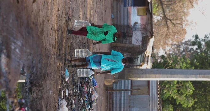 Vertical video.Poverty.Inequality. Climate change.Close-up of two young black African children carrying water for domestic use. Poor living conditions and no access to clean running water.