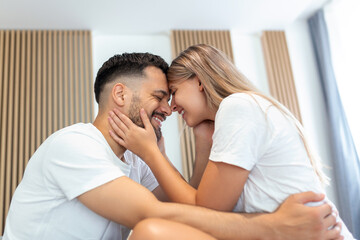 Affectionate young attractive couple sharing a romantic moment in the bedroom at home. Happy young couple hugging and smiling while lying on the bed in a bedroom at home.