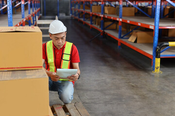 Warehouse worker man with saftyhat and reflective jacket checking list or control large box package for delivery to production stock and inventory in retail warehouse logistics, distribution center