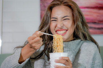 Asian woman enjoy eating hot instant noodles alone in the living room after house work.