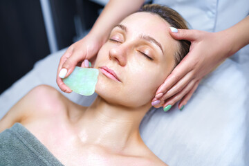 Obraz na płótnie Canvas Woman having an gua sha facial massage with natural jade stone massager in the salon