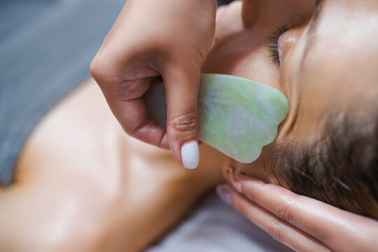 Woman having an gua sha facial massage with natural jade stone massager in the salon