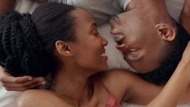 Couple kiss, happy and above love in bedroom, people in happiness in the morning and relax together in bed of home. Top view face of young and African man and woman kissing with smile in house