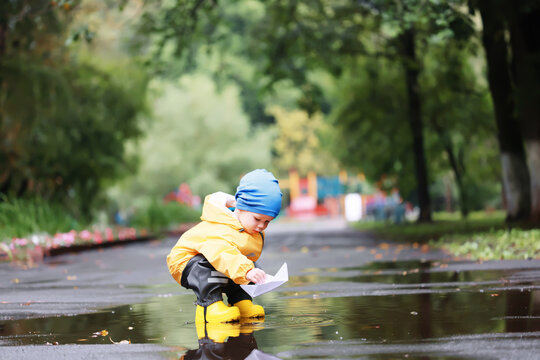 paper boat puddle game, boy seasonal autumn look raincoat, yellow rubber boots, outdoor game