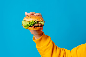 Male hand in yellow clothes hold hamburger on blue background
