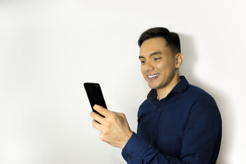 Hombre latino sonriente usando camisa azul, mirando teléfono.