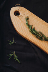 Cooking background concept. Close view of wooden cutting board with rosemary on dark background