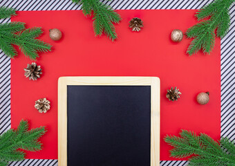 Black chalk board for announcement with spruce branches, golden cones and walnuts, glitter balls on red background and striped. Christmas, New Year flat lay. Copy space