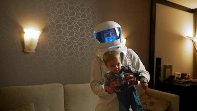Astronaut dances with his son during a vacation at home. A man in an astronaut's helmet with blue backlight spends time with a child.