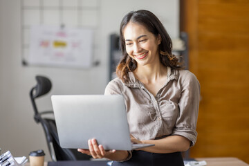 Smiling Happy indian Asian businessman standing and  holding a laptop in workplace an home office.