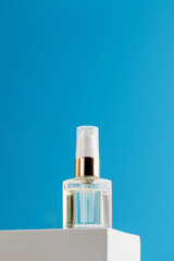 Face serum in a glass container on a podium on a blue background.