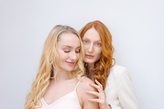 Beauty picture gorgeous happy optimistic beautiful blonde and redhead women posing isolated over light wall background talking gossip to each other.