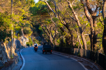 Narrow winding street on Capri island Italy with tall trees on a hot summer evening. Scooter...