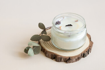 Handmade candle from paraffin and soy wax in glass with wooden wick and dry herbal isolated on pastel beige background. Flat lay, top view, copy space