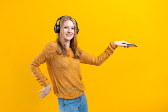 Portrait charming caucasian girl happy smiling during a photo shoot. Stunning young woman in a yellow sweater is relaxing in headphones and dancing funny on a colorful yellow background.