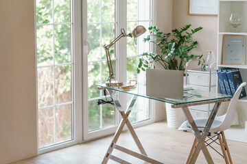 Comfortable workplace with a laptop in the office, at home. Bright room with large windows, bookcase, green plant. Remote work, freelance.