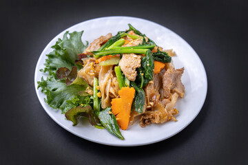 Fried noodles with pork, Thai food for lunch in a plate on black.