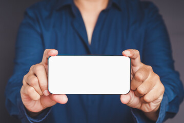 Close-up of hands holding a white blank screen smartphone while standing on a gray background