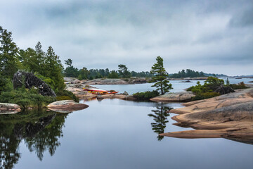 Sea kayaks on a rocky shore by reflective water in Killarney Provincial Park. Shot in the fall. ...