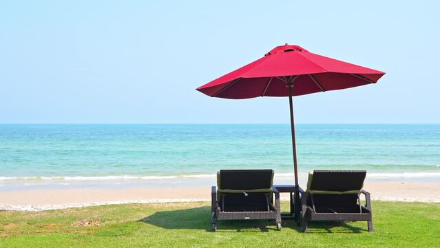 Two empty chaise lounge chairs sitting under a shade umbrella facing the incoming tide. 