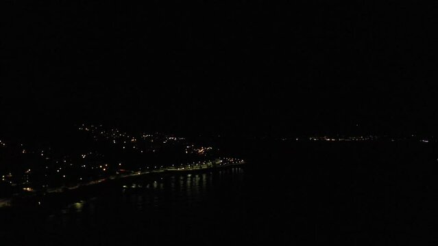 Aerial drone view of the coastline of corsica at night with hail storm at distane and village illuminated 