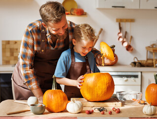 Son and dad making Jack-o-Lantern together at home, carving Halloween pumpkin