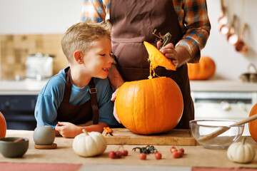 Son and dad making Jack-o-Lantern together at home, carving Halloween pumpkin