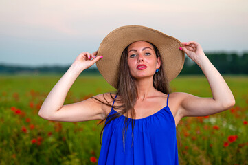 portrait of young woman with long hair and straw hat in poppy field in evening sunlight